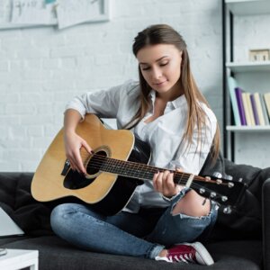 focused girl sitting on couch and playing guitar in living room