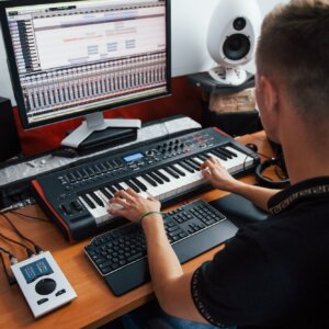 Playing midi keyboard. Sound engineer working and mixing music indoors in the studio