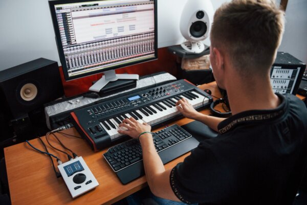 Playing midi keyboard. Sound engineer working and mixing music indoors in the studio