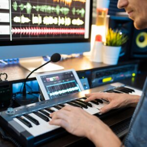 Young musician sitting by workplace and pressing keys of piano keyboard